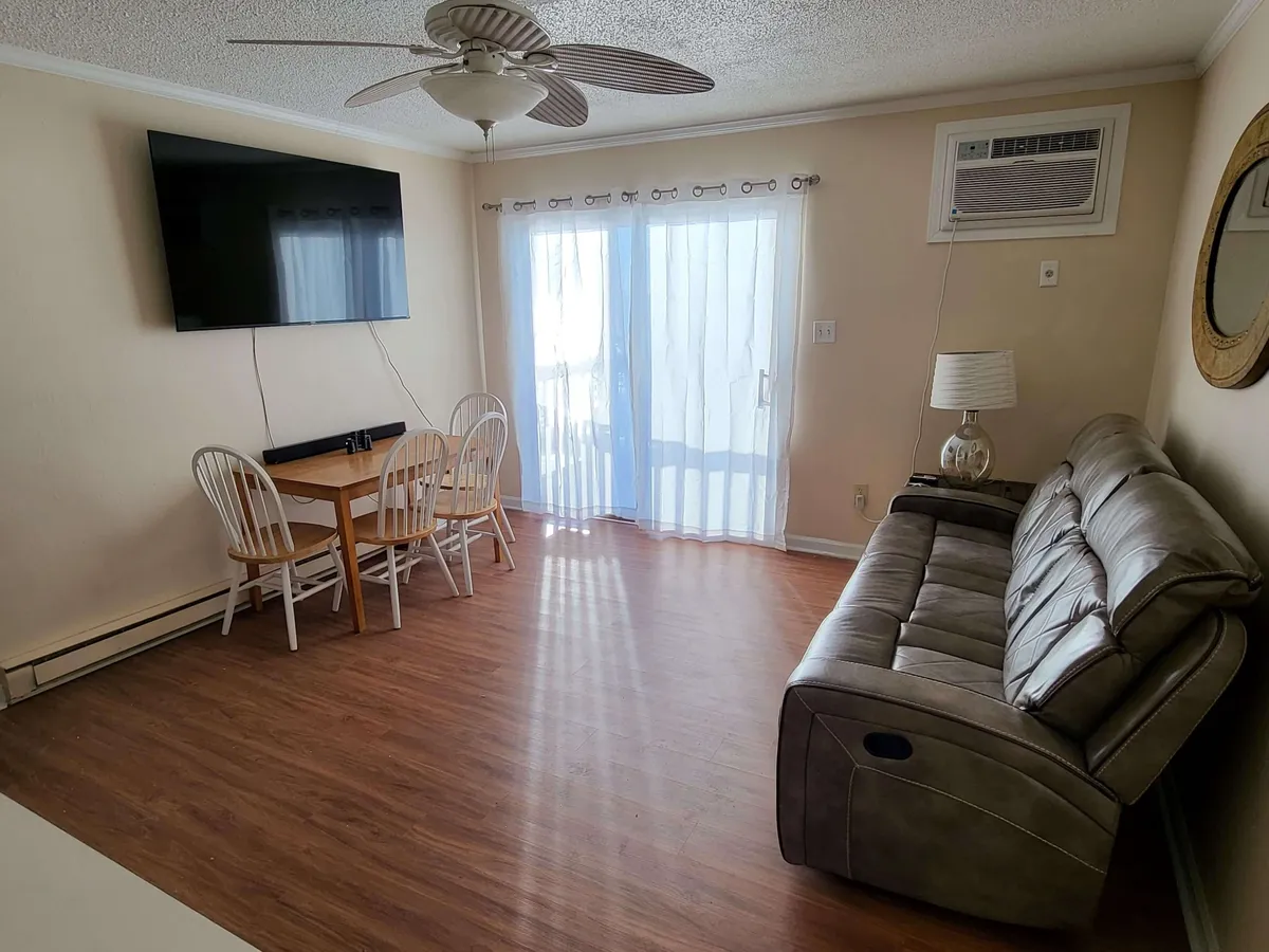 An open-plan room combining a plush sofa, a dining table set near sliding glass doors, and a TV. The abundance of natural light and the cozy arrangement create a comfortable environment for family meals or relaxed mornings.