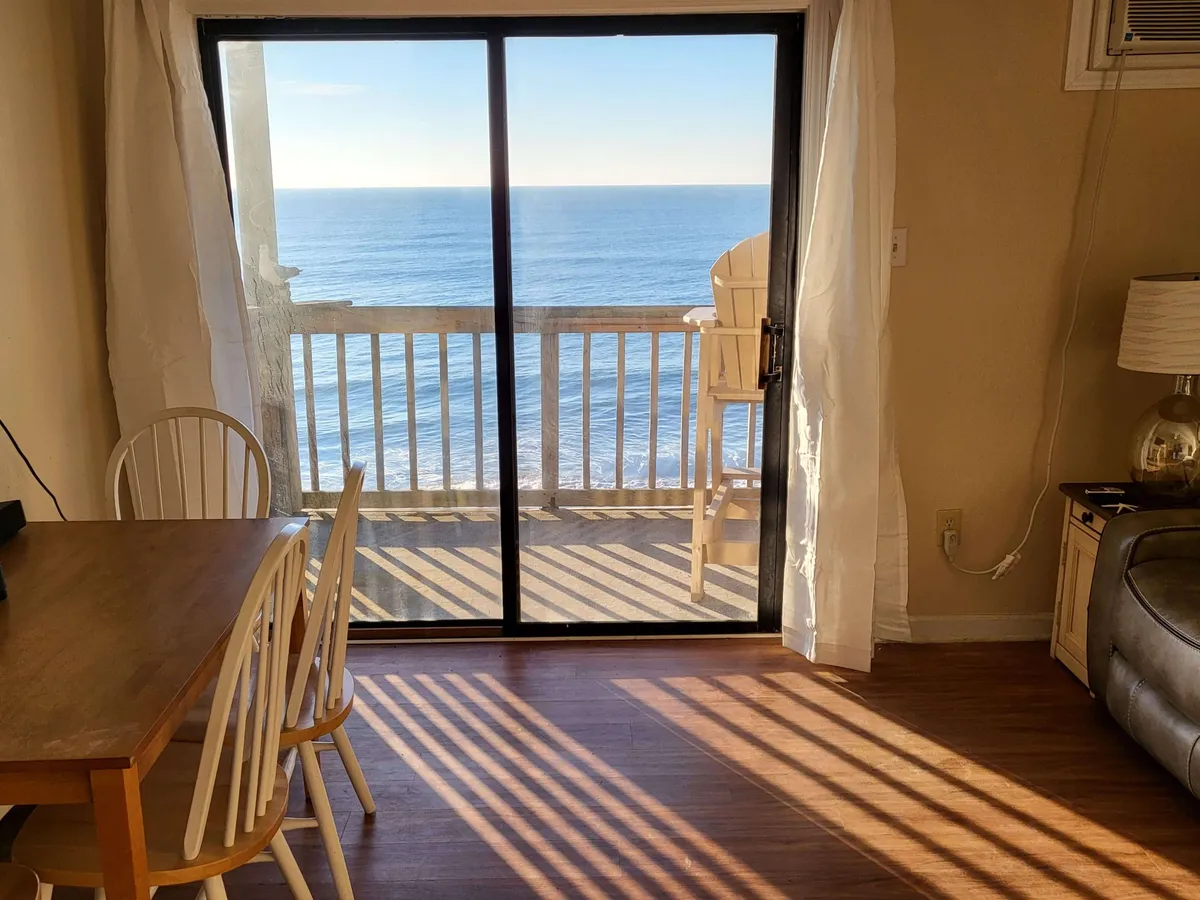 This image features a dining table set close to sliding glass doors, with balcony chairs visible outside. The setup spotlights the inviting ambiance for meals with an ocean backdrop, and highlights the direct access to the private balcony.