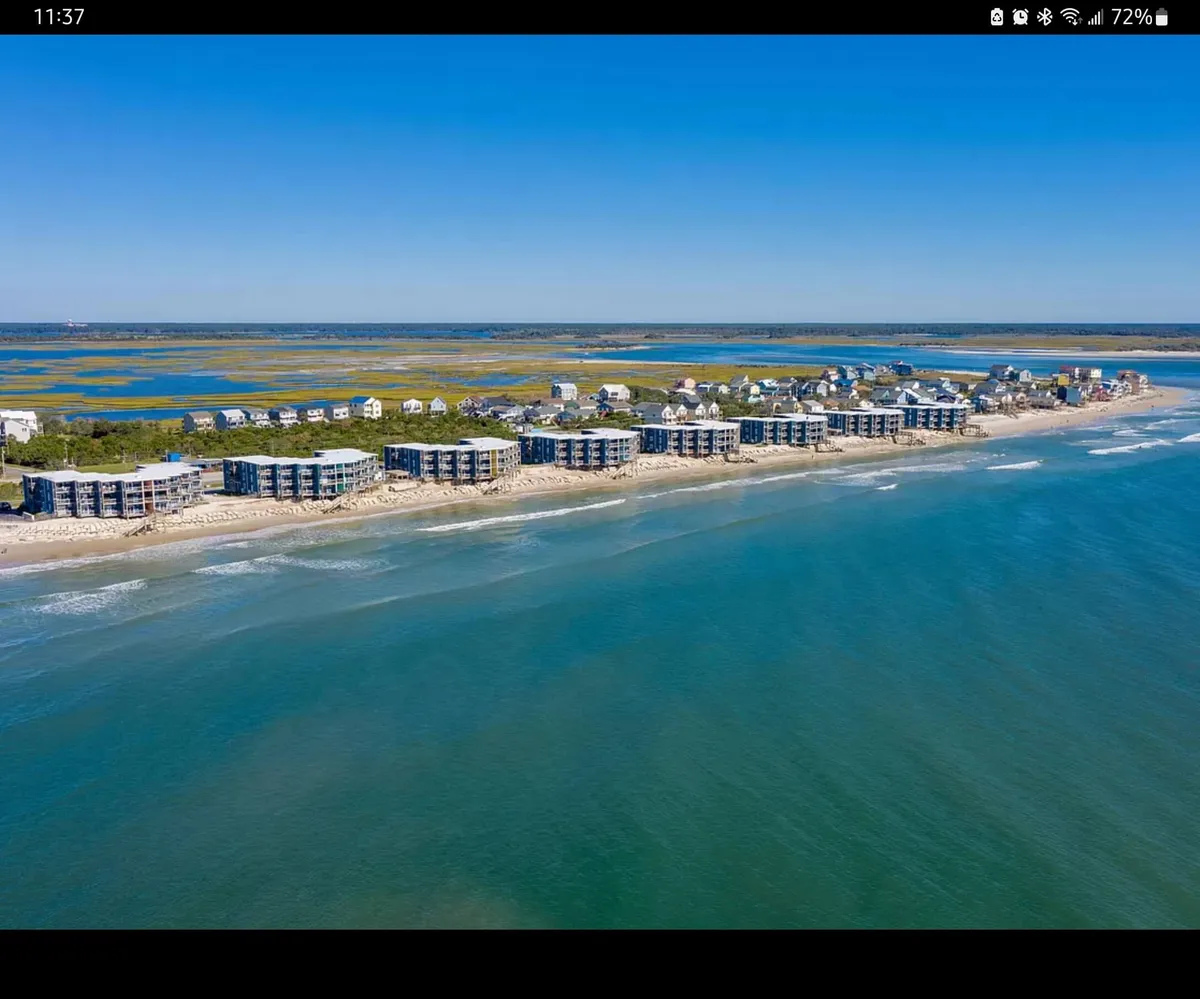 A row of beachfront condos is set against a backdrop of clear blue water and lush greenery. The scene exudes tranquility, with wide sandy stretches of beach inviting long walks or intimate picnics. The balconies offer panoramic ocean views, reinforcing the idea of a private romantic retreat.