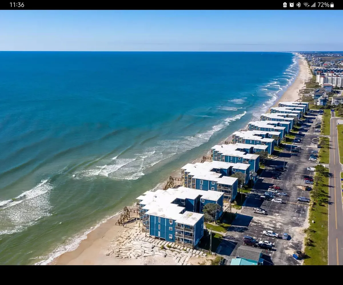 A wide view of beachfront properties nestled along the coast, with ocean waves rolling in and a scenic coastal road nearby. Families are seen enjoying the beach, engaged in activities like sunbathing, water sports, and building sandcastles.