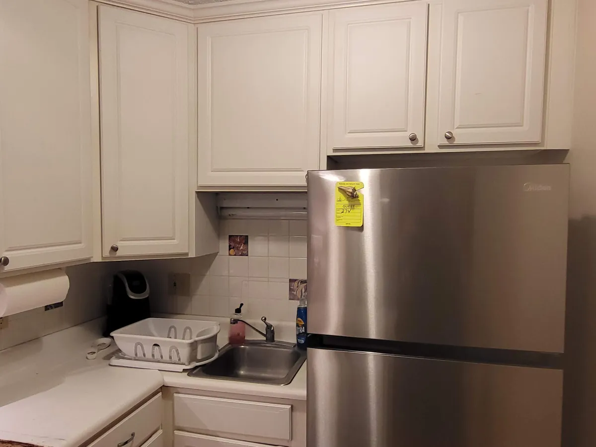 This image showcases a modern kitchen area, featuring a sleek stainless steel refrigerator, crisp white cabinetry, and a convenient sink with a dish rack. The scene feels inviting and practical, highlighting both new appliances and a functional layout perfect for meal prep and easy cleanup.