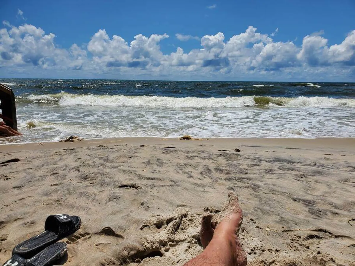 This image captures the serene ocean waves breaking on a sandy beach under a sky dotted with clouds. The tranquil shoreline offers space for sunbathing, swimming, and beachcombing, perfectly evoking the peaceful mood described in the section. The open stretch of sand is inviting for leisurely walks and relaxation, key experiences for seasonal and extended-stay guests.